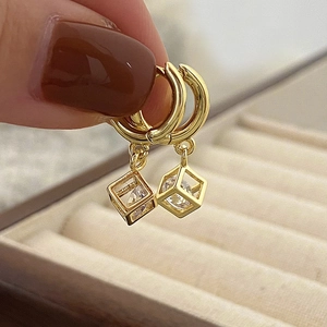 Detail of gold hoop earrings with hollow geometric cube charms and sparkling zircon stones