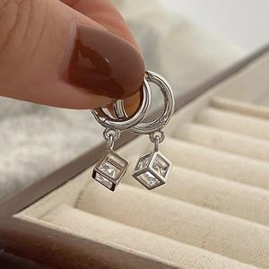 Macro shot of silver geometric cube earrings with square zircon held by a hand
