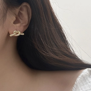 Nahaufnahme goldener Knoten-Ohrstecker mit Zirkonia-Besatz am Ohr des Models