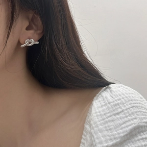 Detaillierte Nahaufnahme eines silbernen Knoten-Ohrrings mit Zirkonia-Kristallen am Ohr