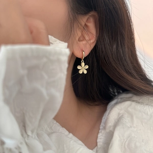 Close-up of elegant gold flower drop earrings with matte texture worn by a model