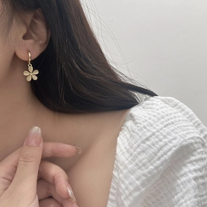 Close-up of elegant gold flower drop earrings with cat eye stones worn by a model