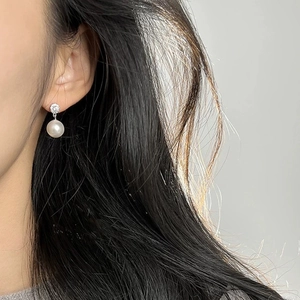 Detailed close-up of a white pearl drop earring with zircon on a female model