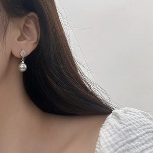 Close-up of elegant pave zircon stud earrings with round grey pearl pendant on model