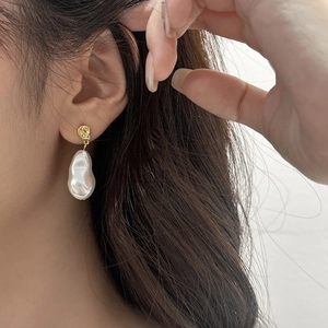 Detailed close-up of Baroque pearl drop earrings with hammered gold metal texture