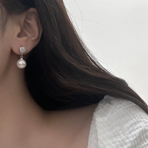 Macro shot of micro-pave zircon stud earrings with white pearl pendants on model