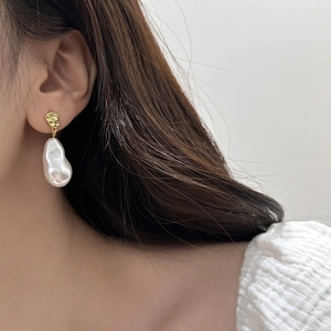 Detail of baroque pearl drop earrings with textured gold studs worn by a model
