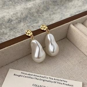 Detailed macro view of baroque pearl earrings with hammered gold studs on beige fabric