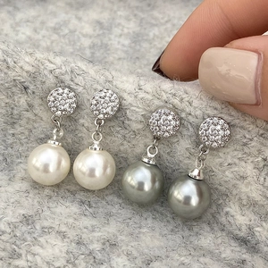 Close-up of pearl drop earrings with sparkling pavé zircons on grey knit fabric