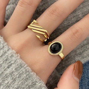 Close-up of stacked gold geometric rings with a black oval stone on model's finger
