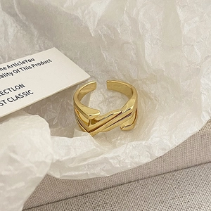 Macro detail of geometric criss-cross golden open ring on white paper background