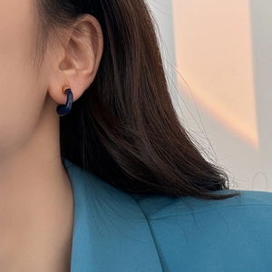 Dettaglio di un orecchino a C in smalto blu indossato con un blazer azzurro elegante