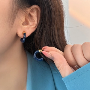 Dettaglio di orecchini a cerchio a C blu scuro con bordo dorato indossati da una modella
