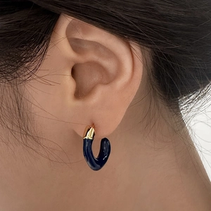 Primo piano di orecchini a C in smalto blu scuro e oro indossati sull'orecchio