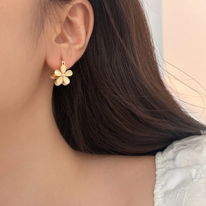 Close-up of elegant gold flower earrings with opal-like petals worn on a model's ear
