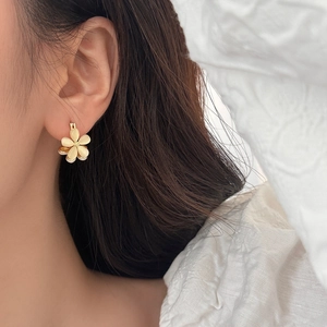 Detailed close-up of a gold flower earring with cream cat-eye petals on a model