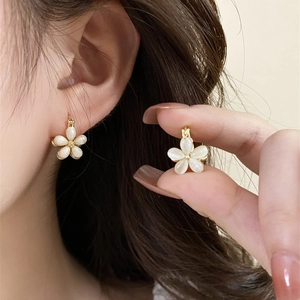 Detail of elegant gold flower earrings with white petals on a model's ear
