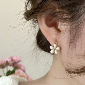 Close-up of floral hoop earring with pearl-white petals and gold center on a female ear