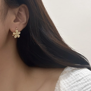 Detail of elegant five-petal flower earring with beige petals and gold metal accents