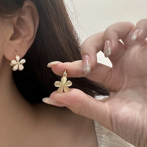 Detail of elegant gold flower earrings with yellow cat eye stone on a model's ear