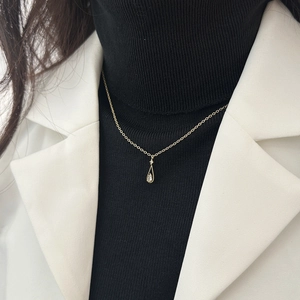 Macro detail of gold-plated waterdrop pendant with zircon on a black turtleneck sweater