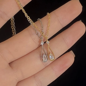 Detailed view of silver and gold teardrop zircon necklaces held in hand against black
