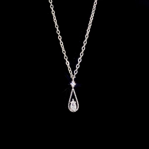 Macro shot of silver pear-shaped zircon pendant with intricate beaded bezel and cross chain
