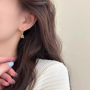 Detailed close-up of a gold-finish woven metal sphere drop earring worn by a model