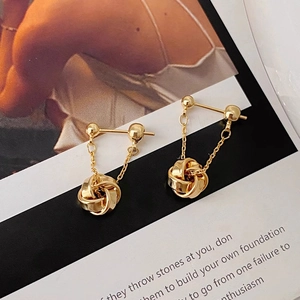 Close-up of gold-plated tassel earrings with chain knot spherical pendants
