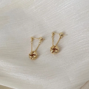 Macro shot of gold tassel earrings with woven metal spheres on pearl silk fabric