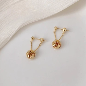 Close-up of golden tassel earrings with woven knot drops and minimalist stud detail