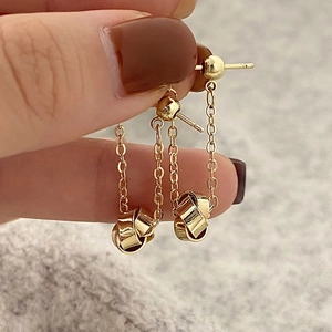 Detail of gold-plated geometric spiral earrings with delicate chain and knot pendant