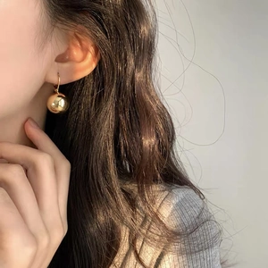 Detailed close-up of minimalist gold spherical drop earrings with a polished mirror finish
