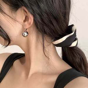 Close-up of polished silver ball earrings paired with a striped scrunchie on a model