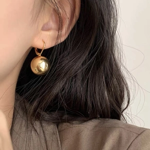 Detailed view of polished gold sphere earrings on a model wearing a brown blazer