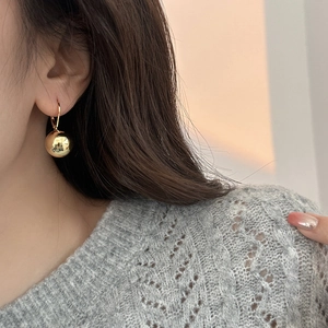 Close-up of a model wearing high-polished gold ball earrings with French hooks
