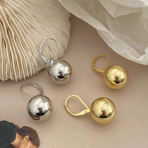 Close-up of polished gold and silver ball earrings on a textured white fabric background