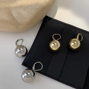 Minimalist gold and silver spherical drop earrings displayed on a black leather pouch