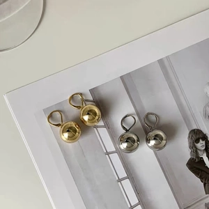 Polished gold and silver ball earrings displayed on a fashion magazine background