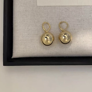 Close-up of gold spherical hoop earrings with a high-polish mirror finish on white fabric