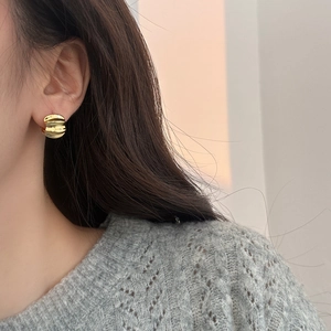 Close-up of a woman wearing gold-toned twisted textured hoop earrings in a minimalist style