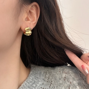 Close-up of gold wavy textured earrings worn by a model showing fluid metallic design