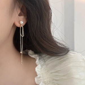 Detail of long gold tassel earrings with white pearl accent on a female model