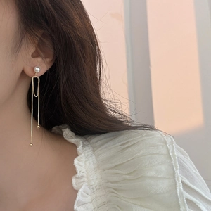 Detail of elegant long tassel earrings with a white pearl and hanging gold chains