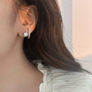 Detail of star-shaped zircon stud and bar earring set worn on model's ear lobe