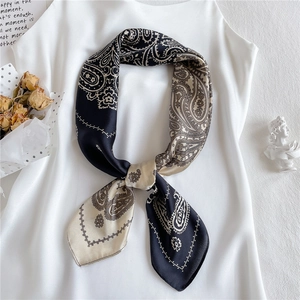 Detail eines schwarz-beigen Paisley-Seidentuchs, elegant an einem weißen Top gebunden