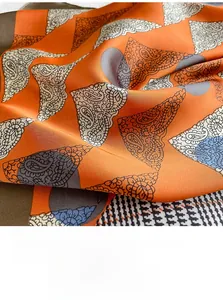 Detailed shot of orange silk scarf showing paisley patterns and houndstooth borders