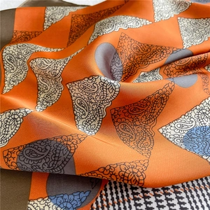Detail of silk-like scarf featuring orange paisley patterns and houndstooth texture