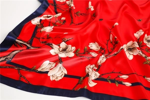 Détail d'un foulard carré rouge au toucher soie avec imprimés de magnolia et bordure satin