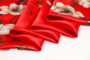 Gros plan du foulard en satin rouge avec motif magnolia blanc et texture soyeuse